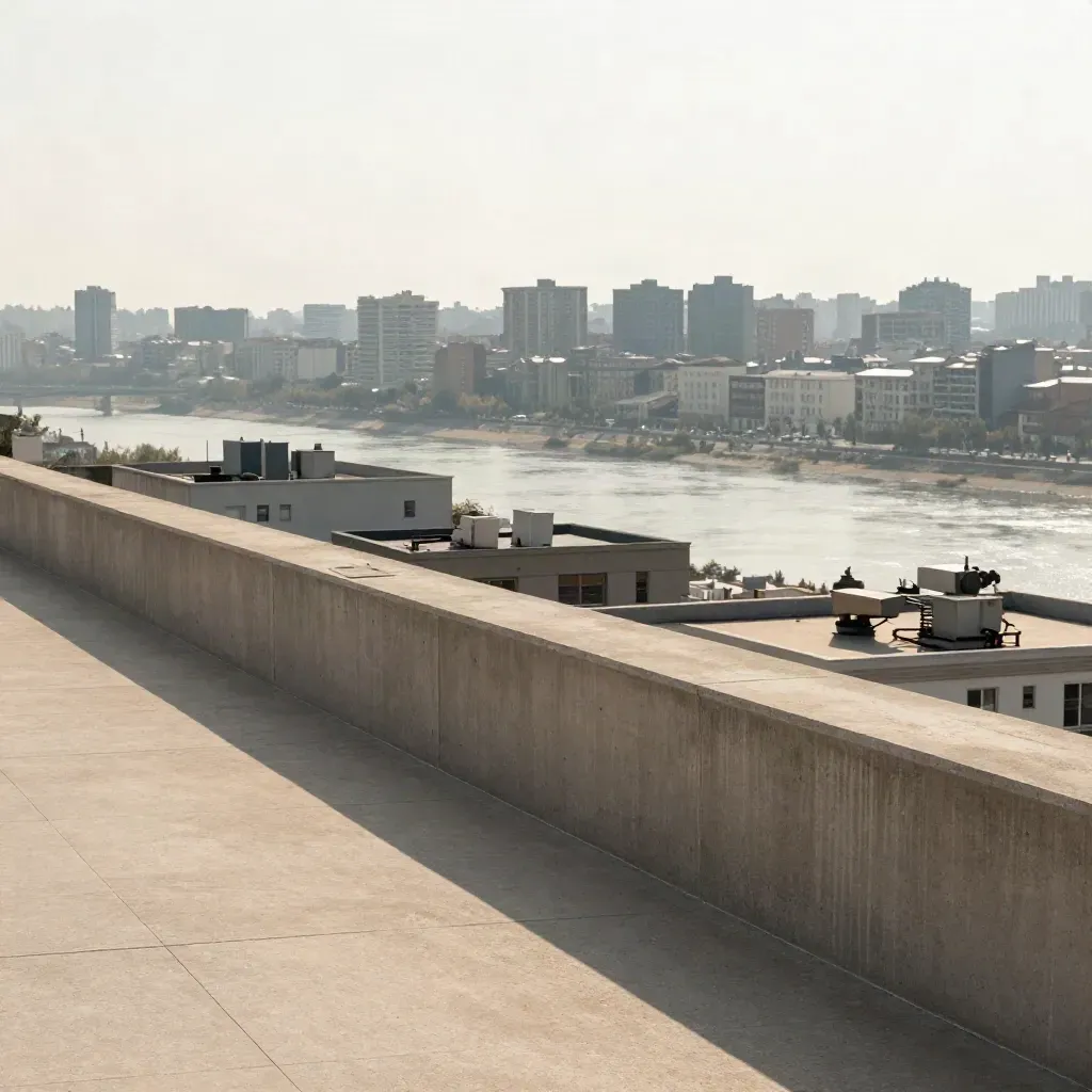 High concrete terrace overlooking layered midrise buildings and a pale river under midday haze.